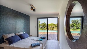 A modern bedroom with a large bed, a view of an outdoor pool, and a unique circular window. - Villa de la Madrague Sea View - 100 m from a small beach - Giens Peninsula 12 P (Hyères)