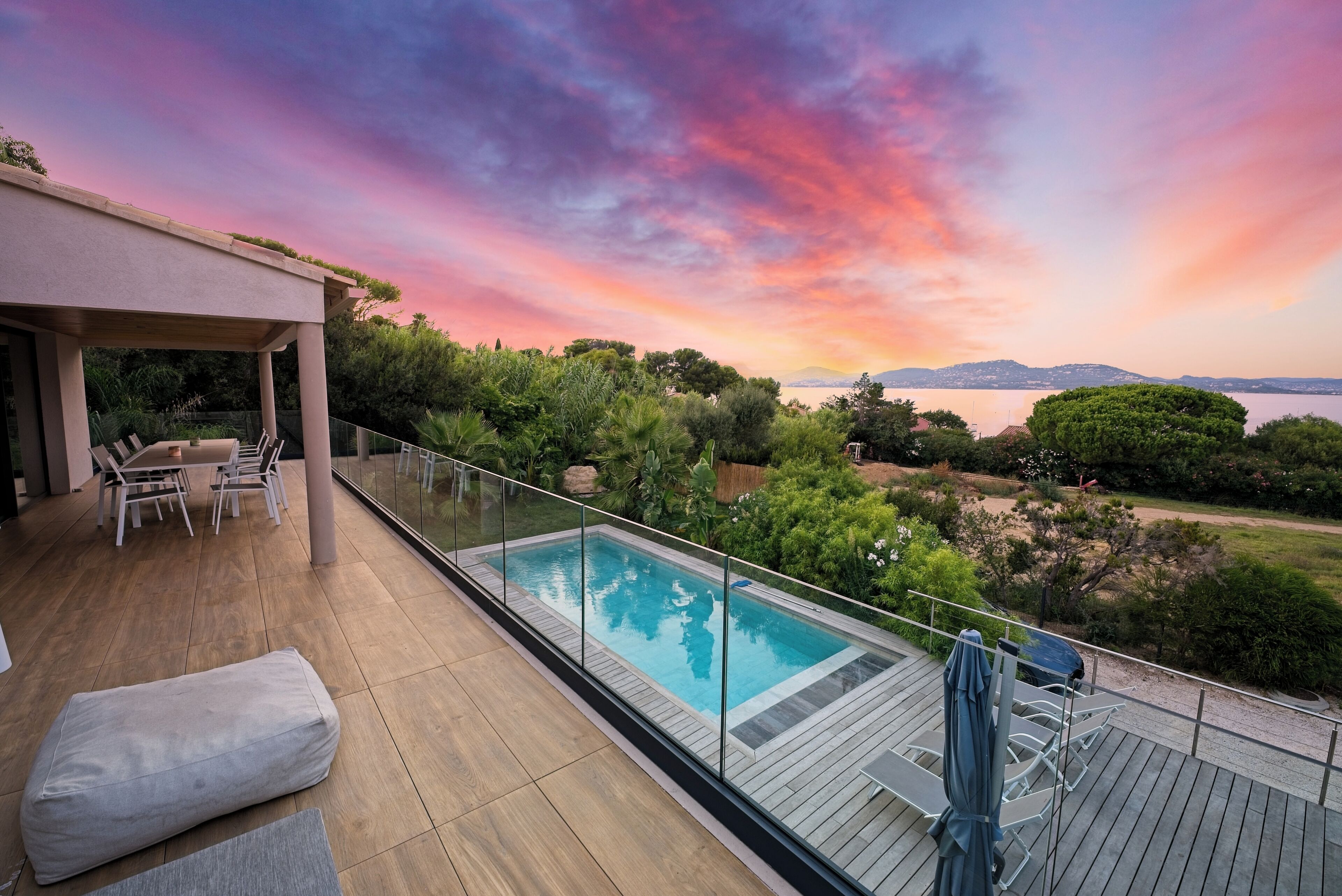 A modern outdoor pool area with a view of the sea and mountains during sunset.
