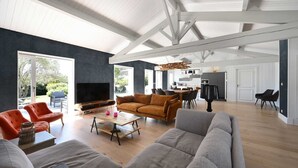 Ein geräumiges Wohnzimmer mit einer großen Couch, einem Couchtisch und einem Fernseher. Es gibt einen Essbereich mit Tisch und Stühlen sowie eine Küche im Hintergrund.