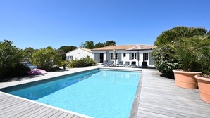 Ein Schwimmbecken mit Liegestühlen, umgeben von Topfpflanzen und einer Holzterrasse.