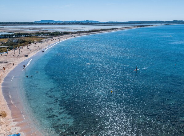 A beach with clear water, a sandy shore, and distant hills.