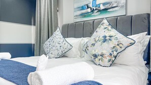 Un lit bien fait, agrémenté d’oreillers à motifs floraux, d’une serviette bleue et d’une serviette blanche.