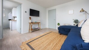 Ein modernes Wohnzimmer mit einem blauen Sofa, einem Fernseher, einem Holztisch und einem Teppich.