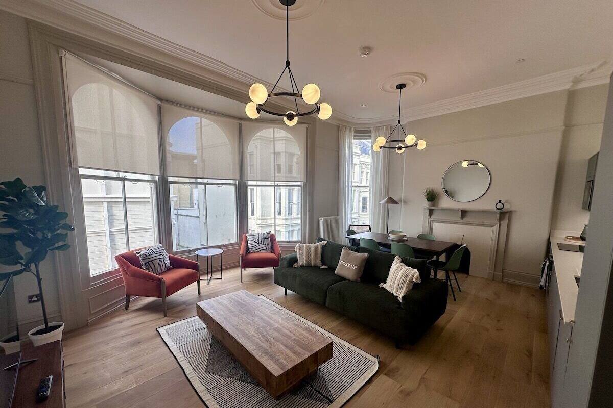 A spacious living room with large windows, a green sofa, a red armchair, and a wooden coffee table.