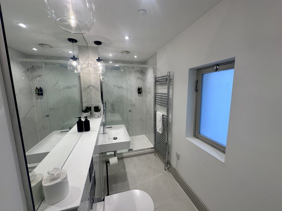 Een moderne badkamer met een douchecabine van glas, een grote spiegel en een raam.