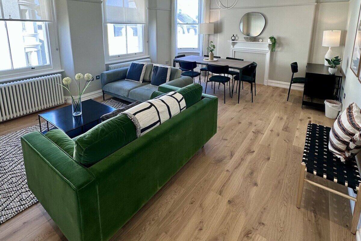 A modern living room with a green sofa, a dining area, and a fireplace.