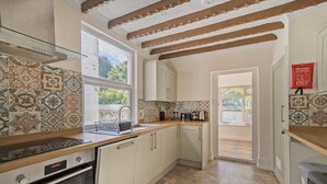 A kitchen with patterned tiles, wooden beams, a window, and a view of greenery. - Admiralty Retreat by Pureserviced (Plymouth)