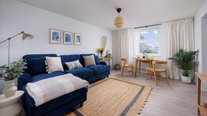 A modern living room with a blue sofa, a dining area, and a large window with curtains. - Luxury Ground Floor 2 bed Apartment (Plymouth)