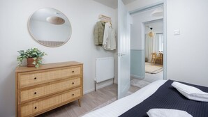 A bedroom with a bed, a dresser, a mirror, and a door leading to another room. - Luxury Ground Floor 2 bed Apartment (Plymouth)