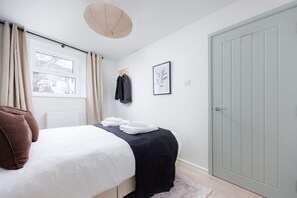 A bedroom with a bed, a window, a door, and a wall-mounted towel rack. - Luxury Ground Floor 2 bed Apartment (Plymouth)