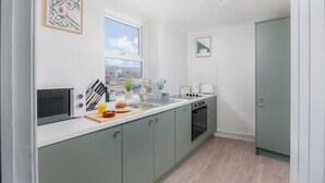 A modern kitchen with a built-in oven, a microwave, and a sink. There is a window providing a view of the city. - Luxury Ground Floor 2 bed Apartment (Plymouth)
