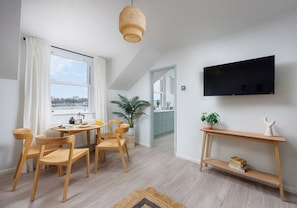 Uma sala de estar moderna com área de jantar, televisão fixada na parede e varanda com vista.