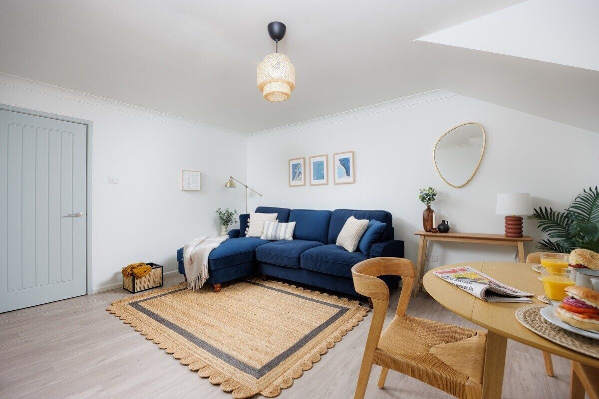 Ein modernes Wohnzimmer mit einem blauen Ecksofa, einem Holzessttisch und einem gewebten Teppich.