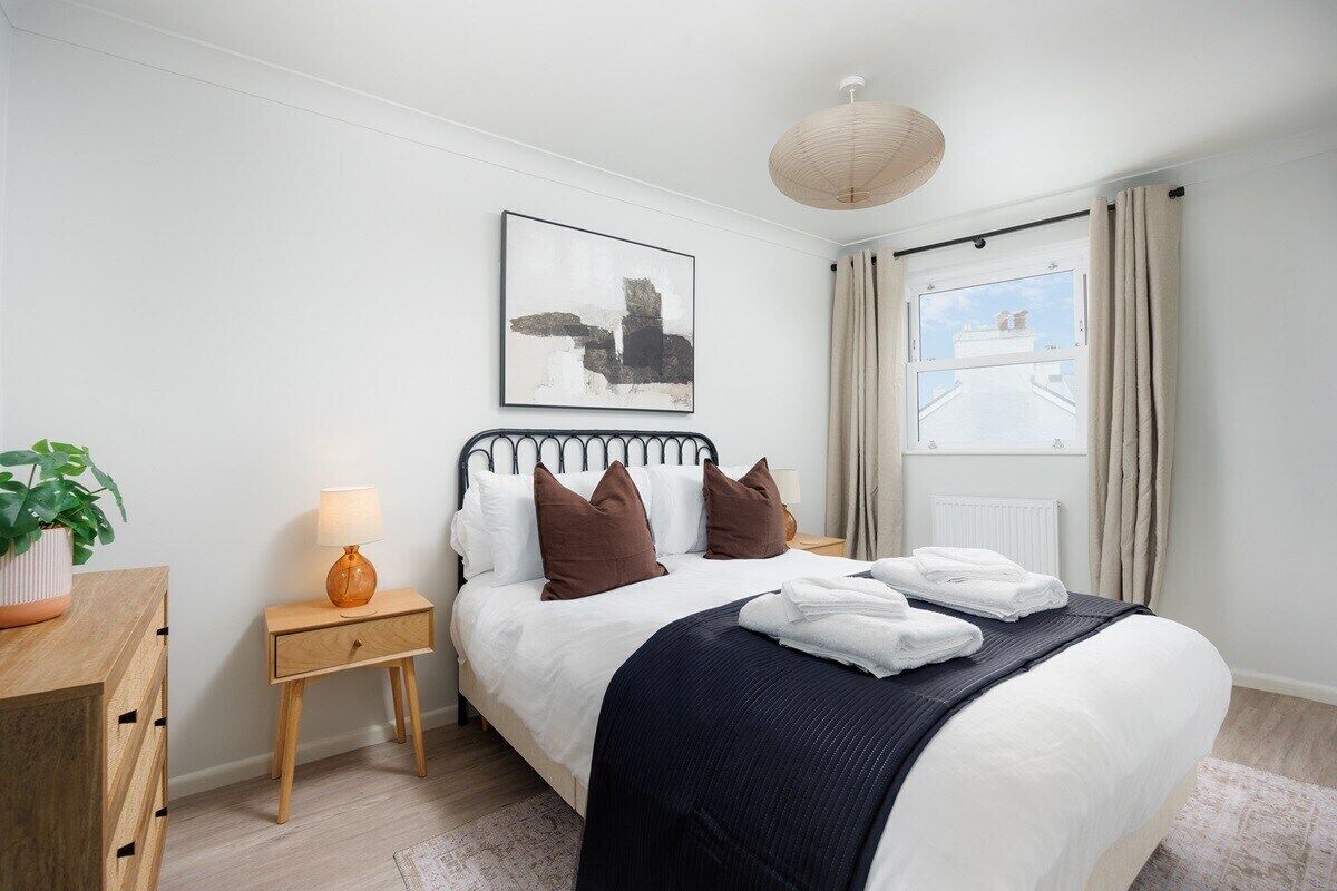 A neatly arranged bedroom with a bed, bedside table, lamp, and a painting on the wall.
