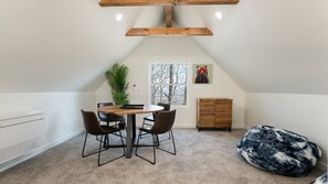Ein gemütliches Dachzimmer mit Holztisch, vier Stühlen, einem Blumentopf, einem farbenfrohen Gemälde und einem Sitzsack.