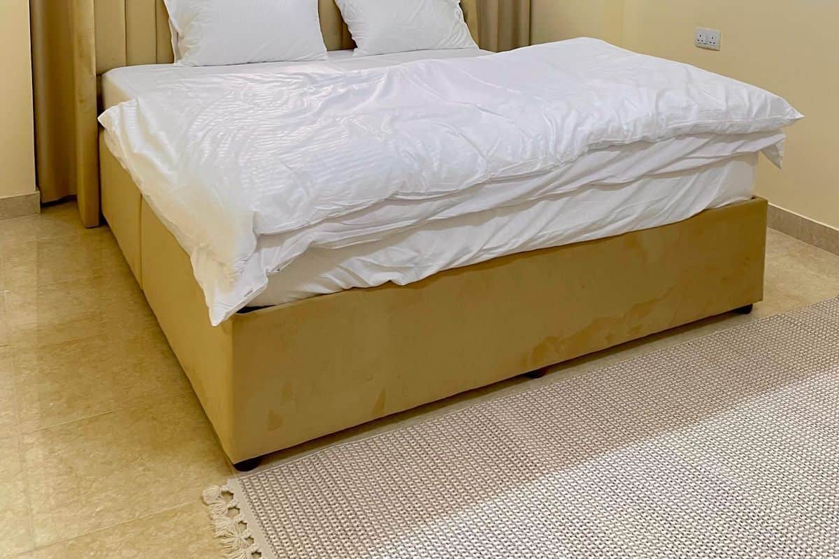 A neatly made bed with white linens in a room with a beige headboard and curtains.