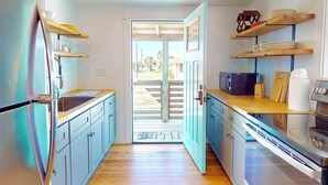 Cozinha com geladeira, micro-ondas e forno, bancadas de madeira e vista por uma porta aberta.