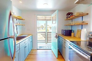 A kitchen with a refrigerator, microwave, and oven, wooden countertops, and a view through an open door.