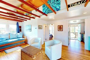 A spacious living area with a sofa, chairs, and a wicker ottoman. There is a ceiling with exposed beams and a sign that reads 'TOBACCO'.