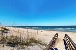 A beach with a wooden boardwalk leading to the water, sandy dunes, and sparse vegetation.