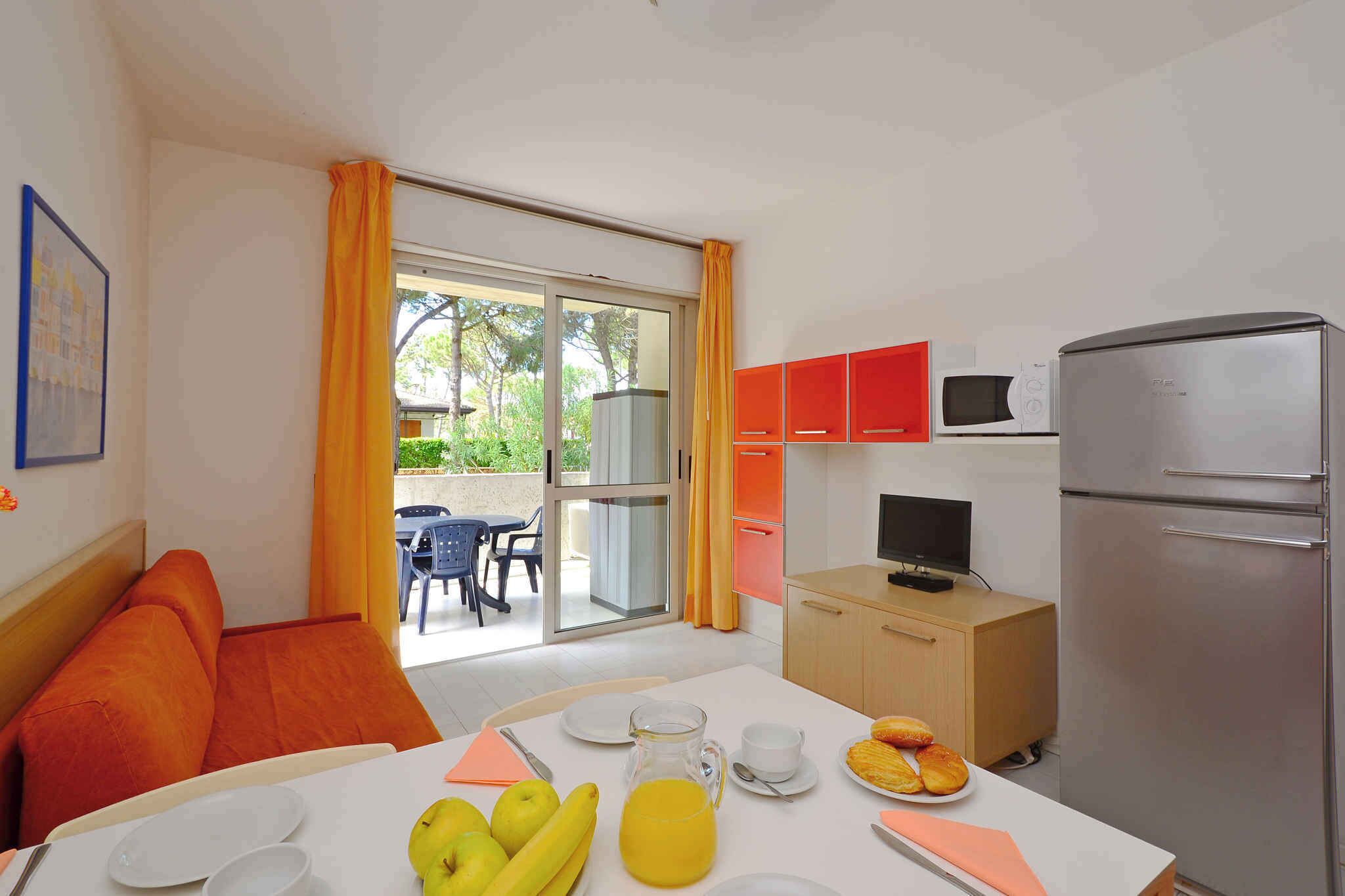 A compact hotel room with a dining area, a kitchenette, and a sliding glass door leading to an outdoor seating area.