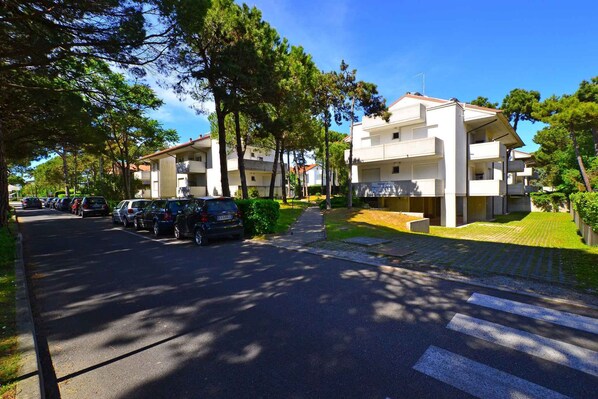 A multi-story residential building with a parking area in front. - Holiday apartment with air conditioning, balcony and pool (Lignano Sabbiadoro)
