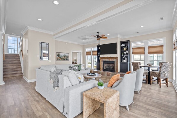 A spacious living room with a fireplace, a dining area, and a staircase leading to an upper level. - Fantasea #183 - 7 BD Oceanfront Home, Pet-Friendly w/ Hot tub! (North Topsail Beach)