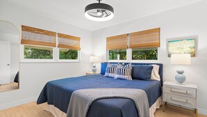 A bedroom with a large bed, two bedside tables, a ceiling fan, and a window with a view of greenery. - 3-bedrooms-2 Full Baths,  Private backyard, mnts to Central Beach & downtown (Vero Beach)