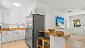 A modern kitchen with white cabinetry, a stainless steel refrigerator, a wooden stool, and a kitchen island with a bowl. - 3-bedrooms-2 Full Baths,  Private backyard, mnts to Central Beach & downtown (Vero Beach)