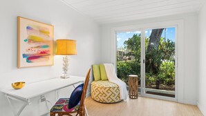A modern room with a white desk, colorful cushions, a patterned ottoman, and a large window with a view of greenery. - 3-bedrooms-2 Full Baths,  Private backyard, mnts to Central Beach & downtown (Vero Beach)