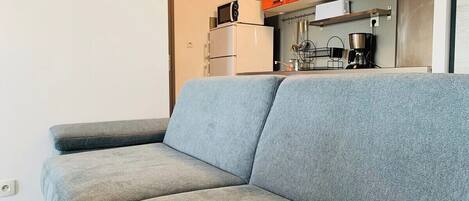 Un sofá gris en una cocina moderna con armarios naranja y electrodomésticos blancos.