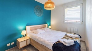Un dormitorio con cama, mesitas de noche, lámpara colgante, un adorno en la pared y una ventana con vistas.