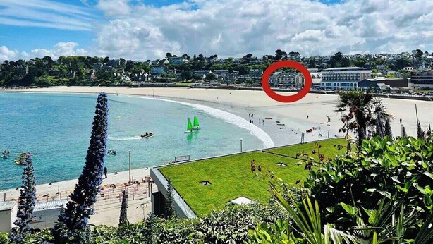 Vista costera con playa, veleros y un edificio marcado en rojo.