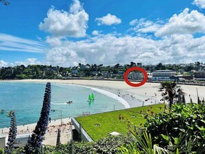 Udsigt over kysten med strand, sejlbåde og en bygning markeret med rødt.