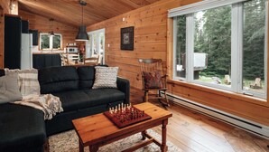 Interior acogedor de una cabaña con detalles de madera, un comedor y un ventanal que ofrece vistas al bosque.