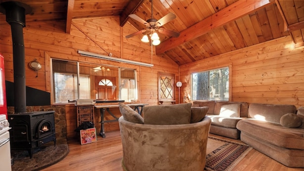 A cozy cabin interior with a stone fireplace, wooden walls, a ceiling fan, and a comfortable seating area. - Charming Mountain Getaway (Sugarloaf)