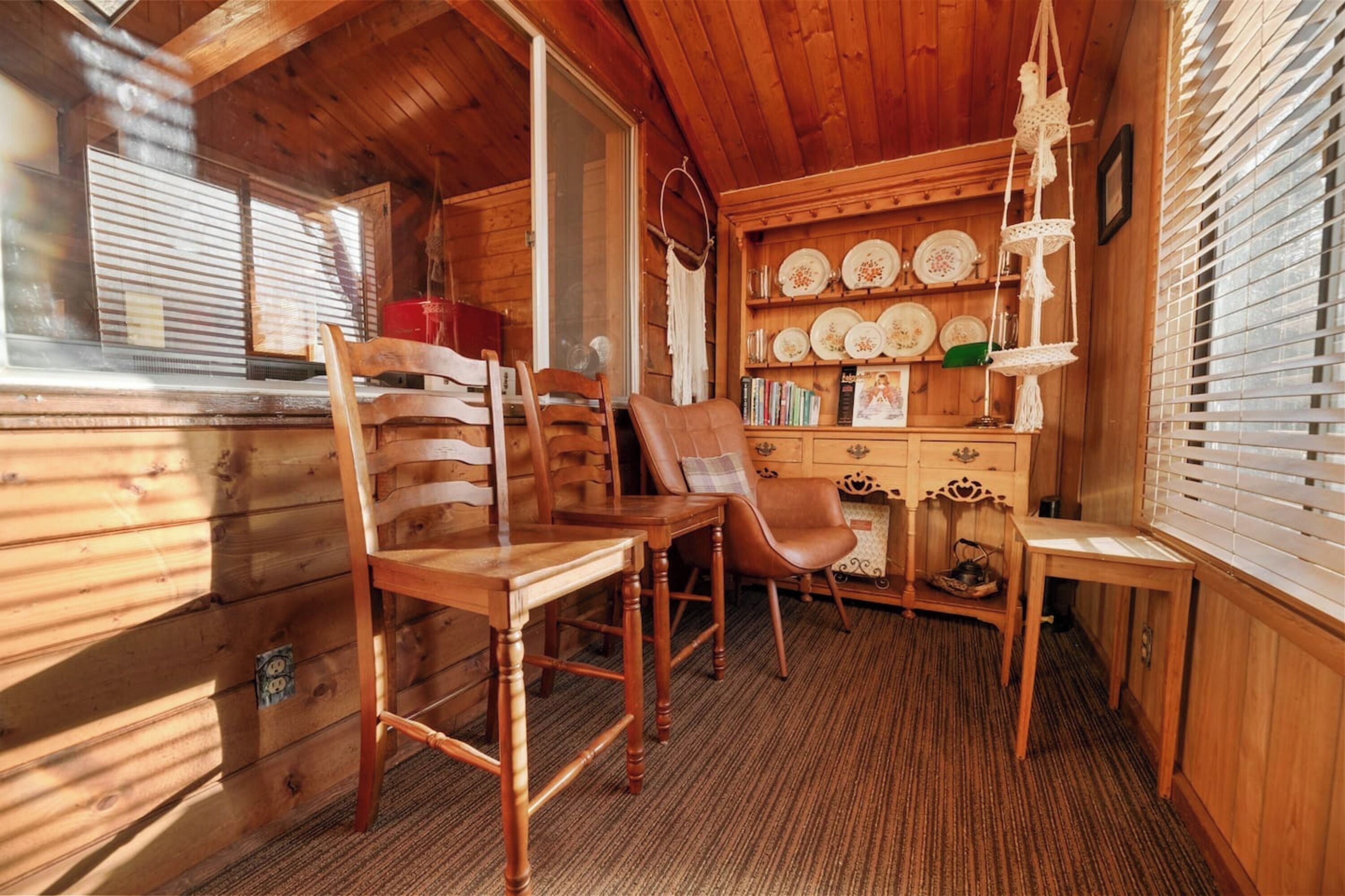 Een houten chaletinterieur met een eethoek, houten stoelen, een tafel en een plank met borden en boeken.