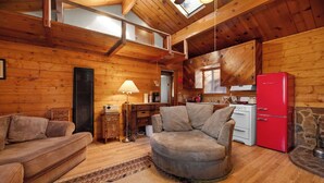 A cozy cabin interior with wooden walls, a sofa, a chair, a dining table, and a red refrigerator. - Charming Mountain Getaway (Sugarloaf)