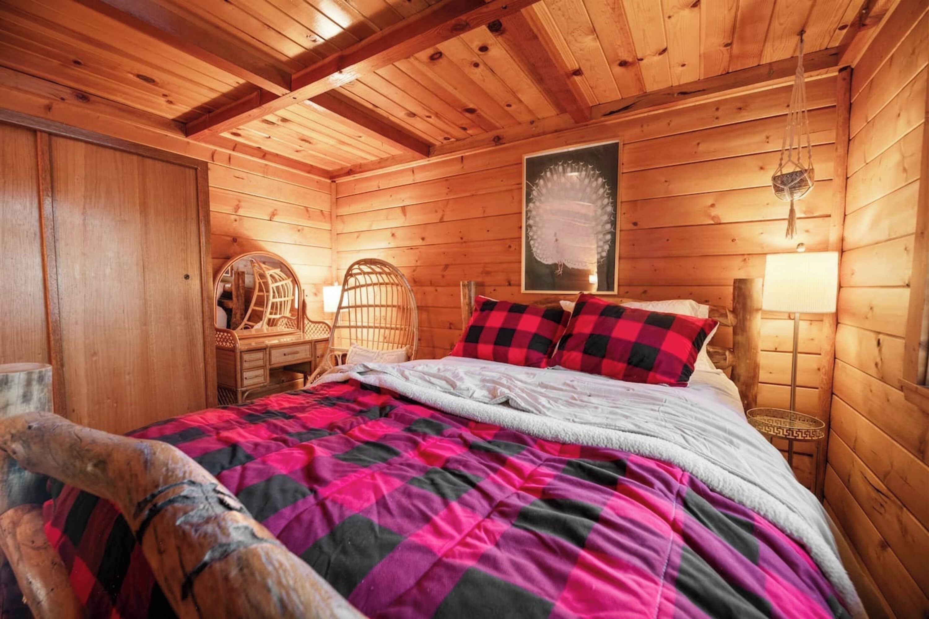 Een gezellige houten kamer met een bed, een houten stoel, een klein tafeltje en een hanglamp.