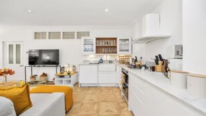 Une cuisine moderne avec des meubles blancs, un four encastré et un plan de travail équipé d’ustensiles de cuisine.