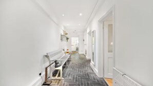 Un couloir étroit avec un sol à motifs en chevrons, des murs blancs et un banc sur lequel est posée une lampe.