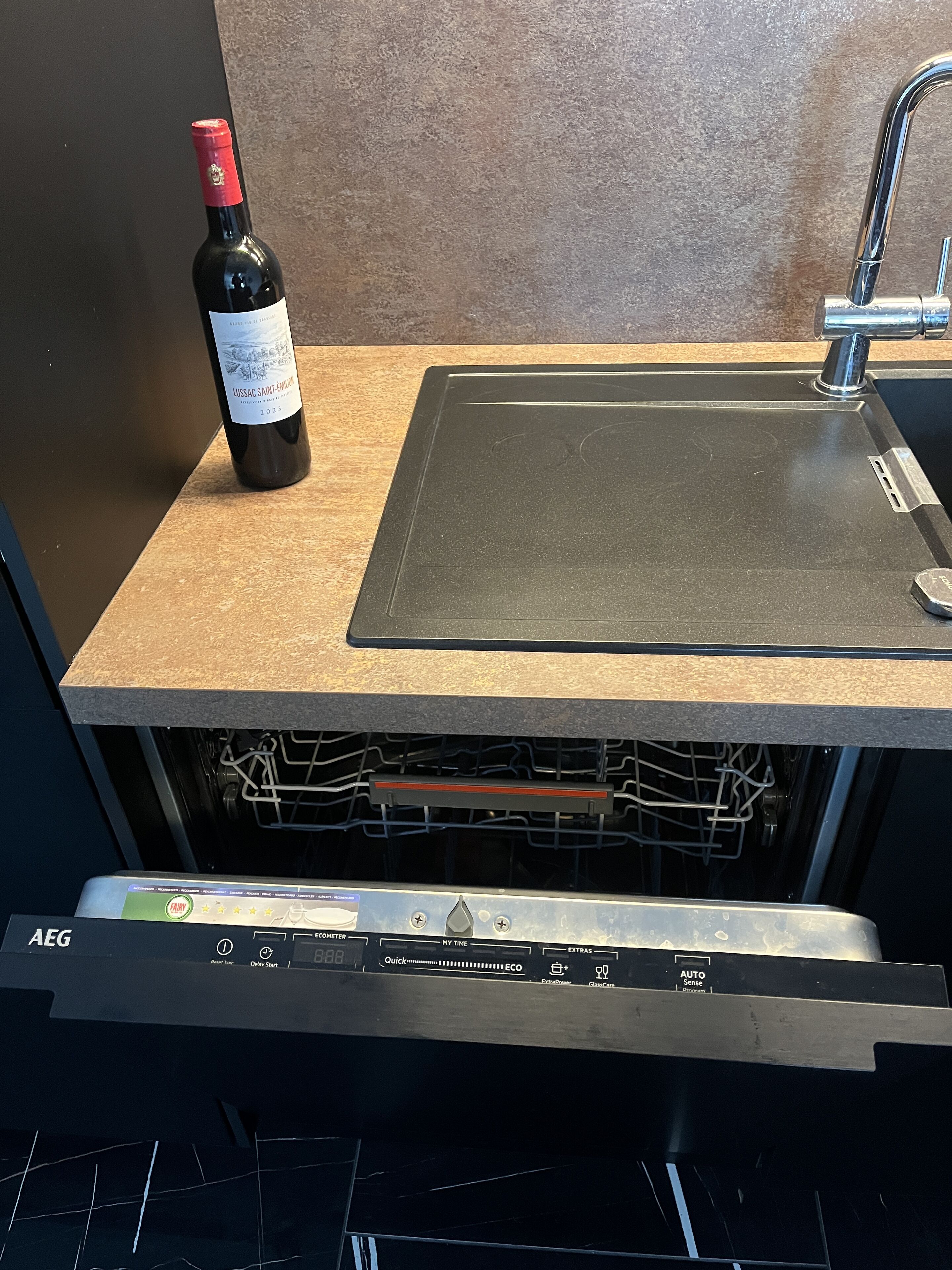 A kitchen with a wine bottle, a sink, and a dishwasher.