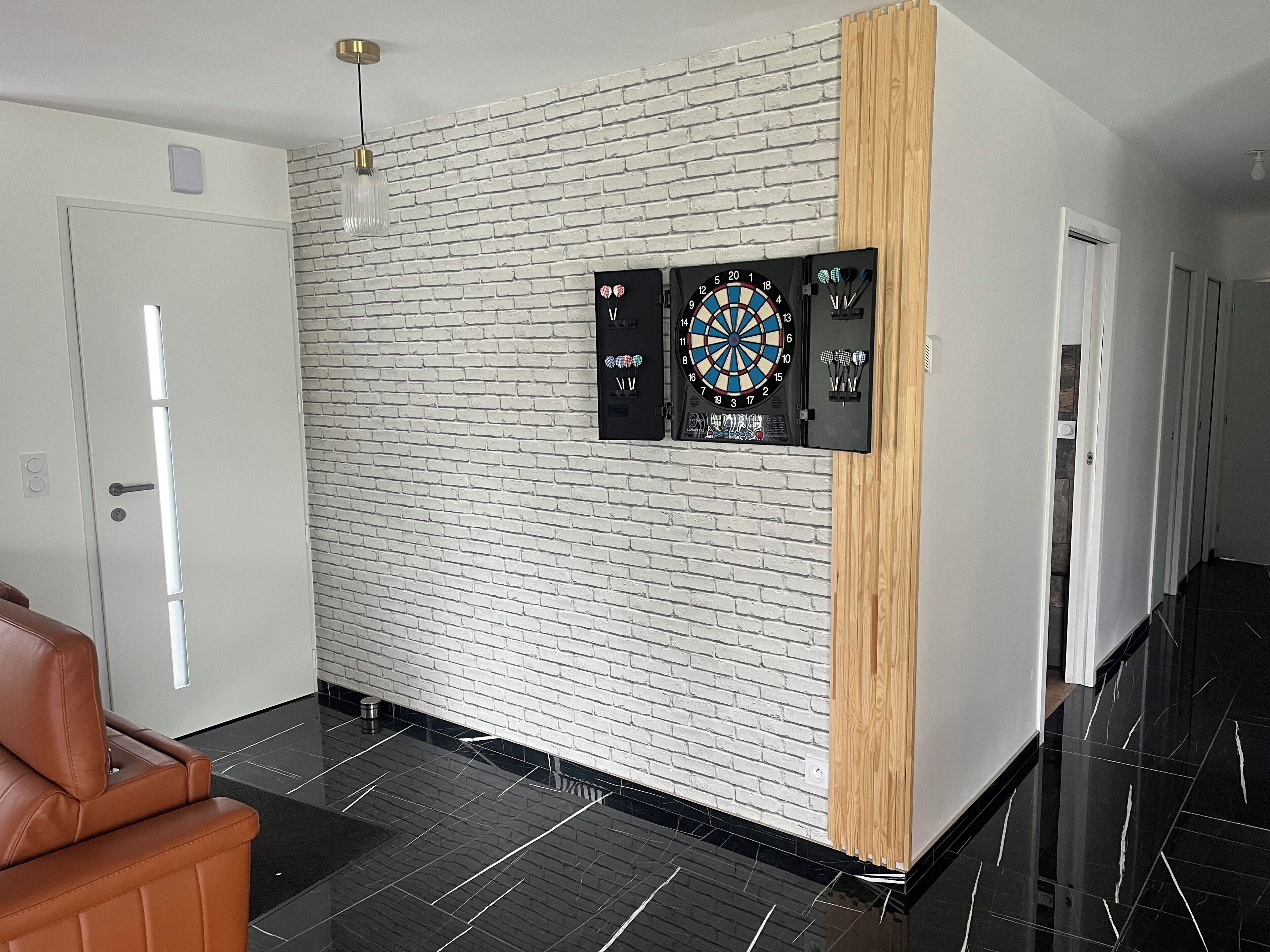 A modern interior with a brick wall, a dartboard, and a leather sofa.