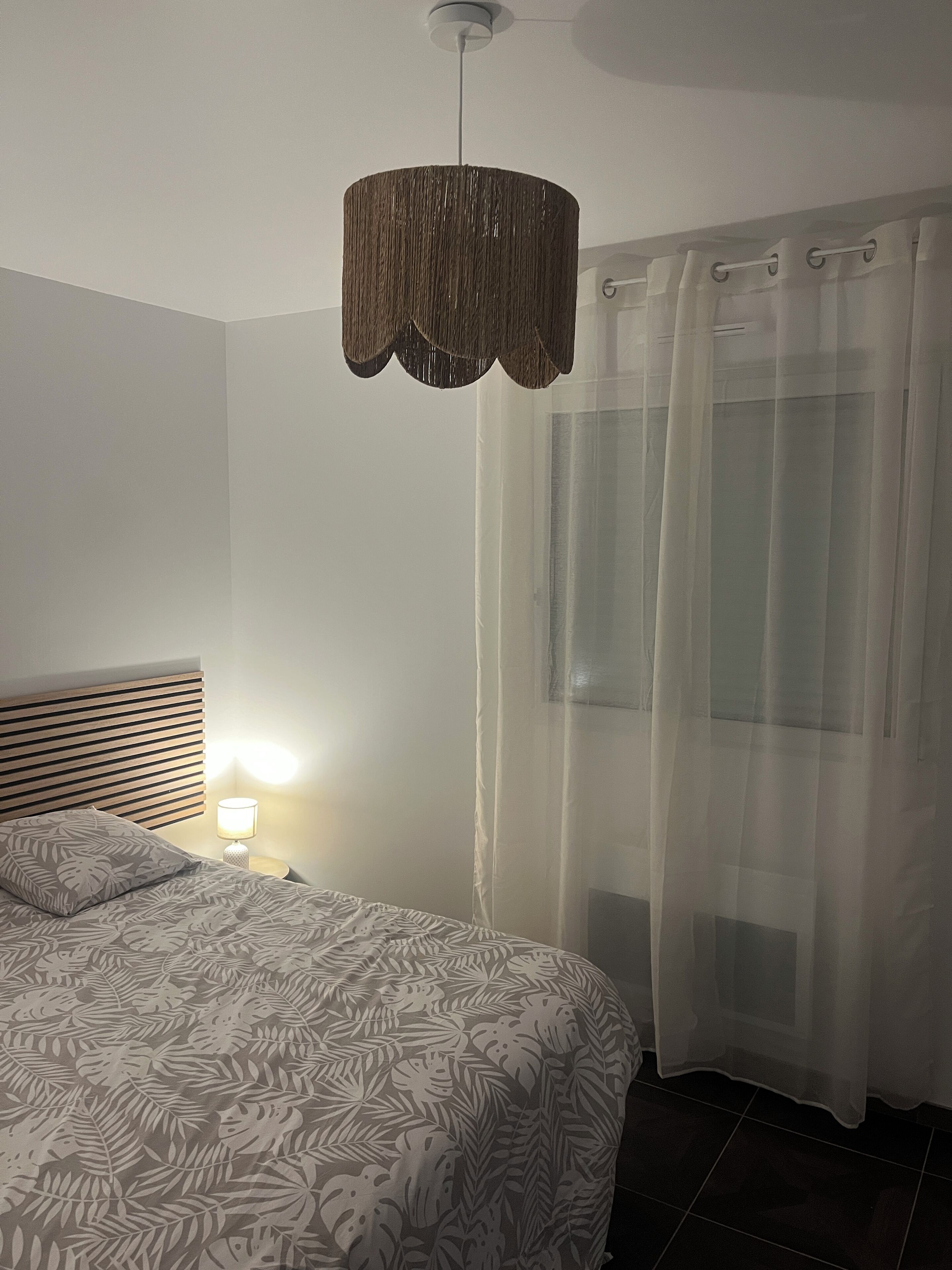 Een slaapkamer met een bed, een bedlamp, een hangende lamp en dunne gordijnen.