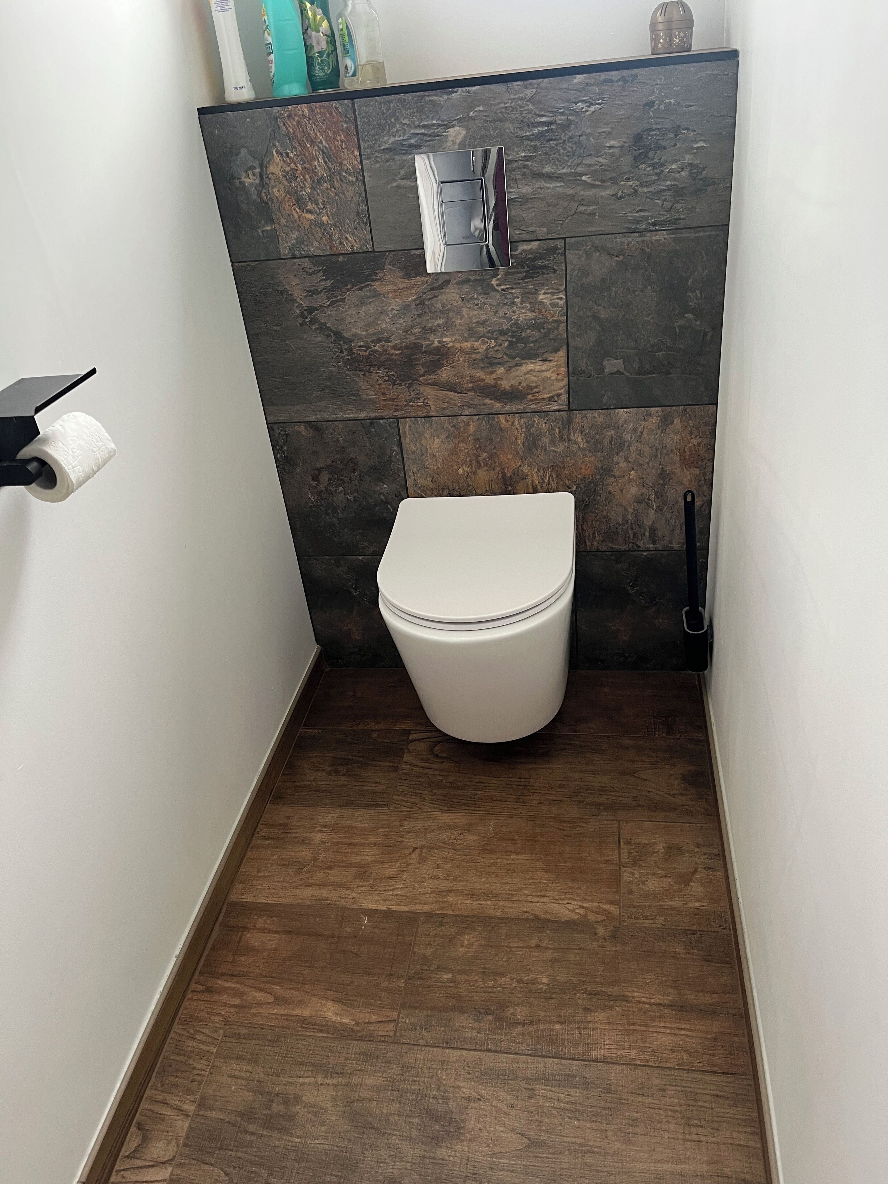 A small, modern bathroom with a white toilet, dark wood flooring, and a stone backsplash.