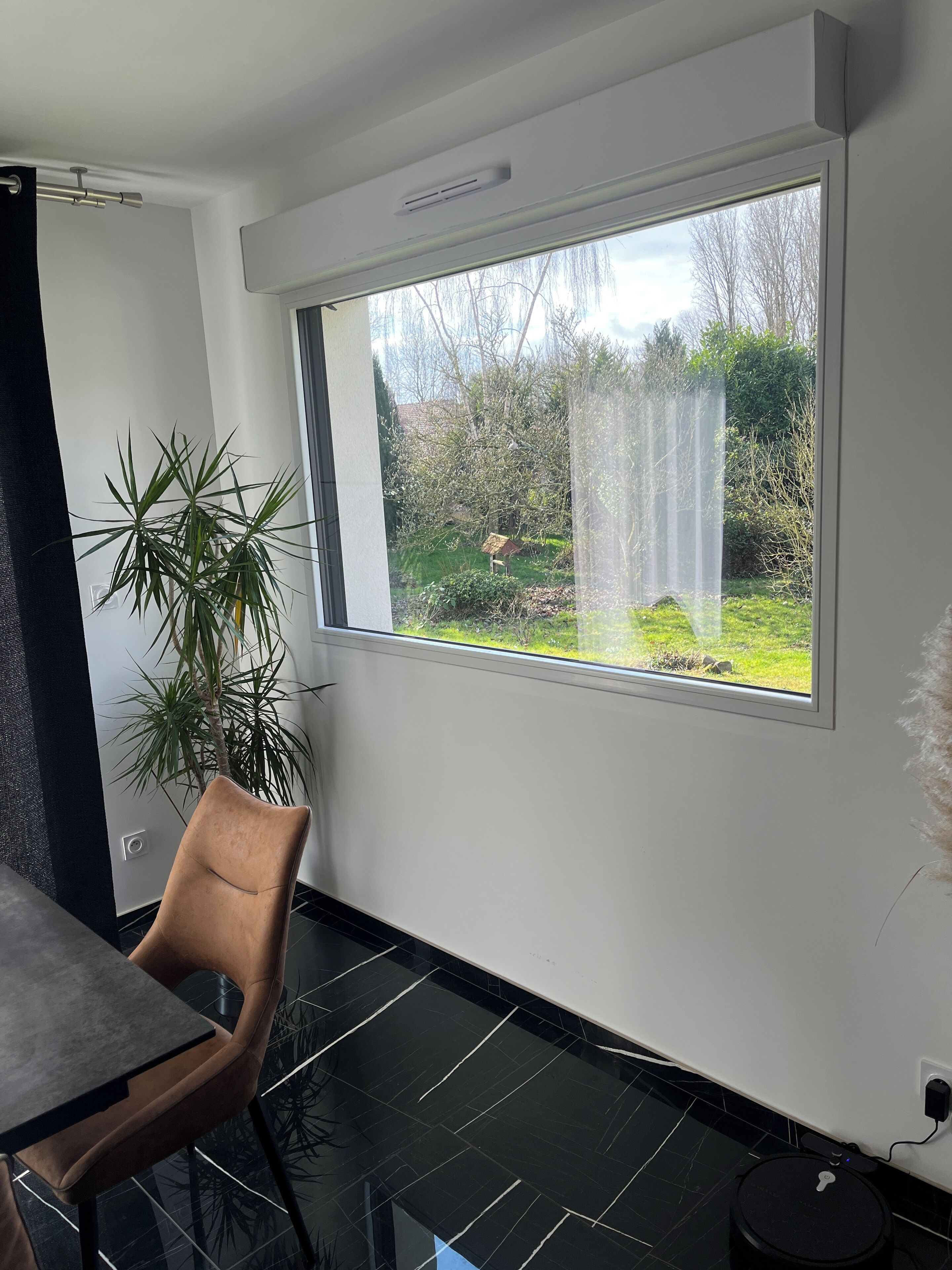 A modern room with a large window, a dining table, a chair, and a potted plant.