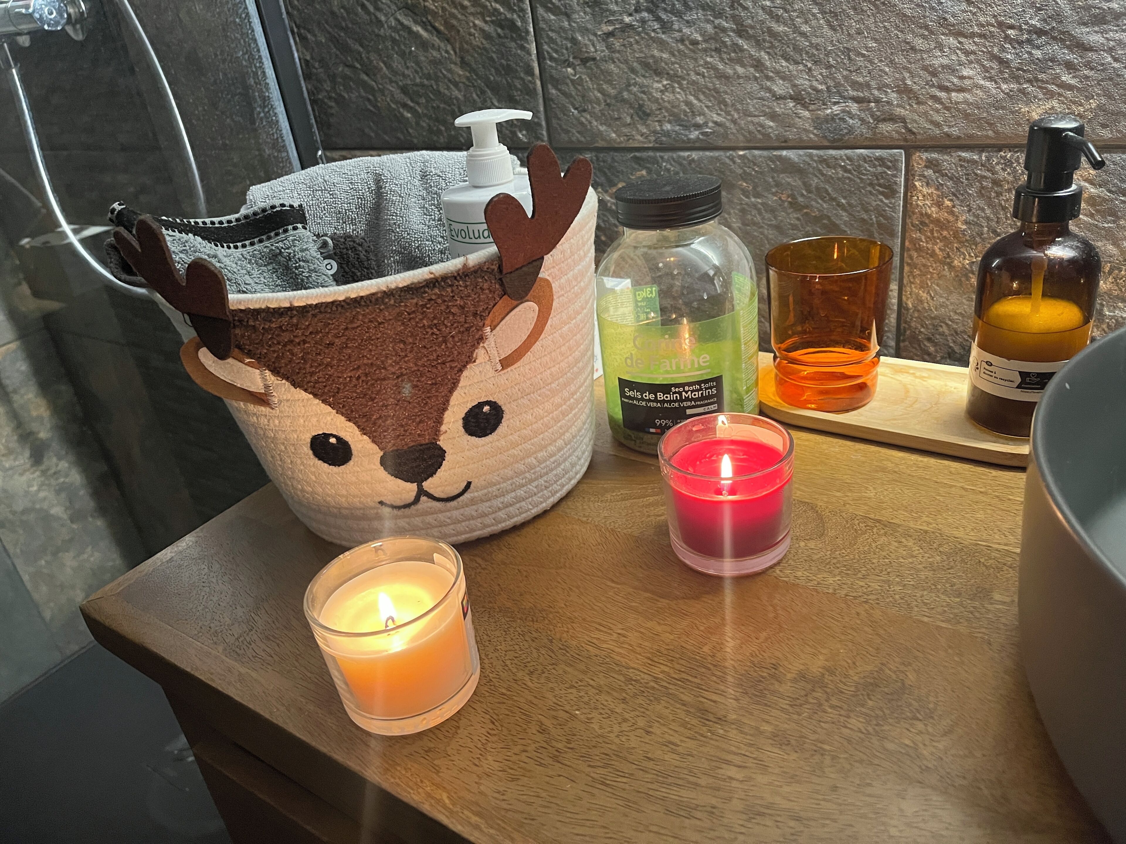 Una encimera de baño con un bolso mullido con forma de animal, una vela y varios artículos de aseo.