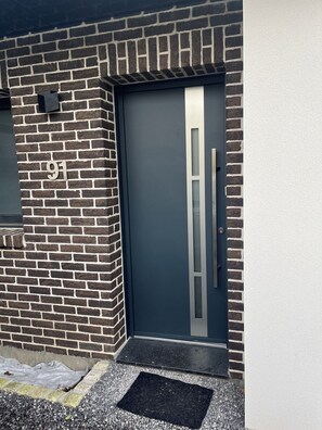 A modern building entrance with a dark door, a metal handle, and a number '91' on the brick wall. - La Maison 91  (Croix-en-Ternois)
