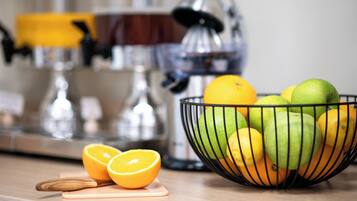 A kitchen counter with a fruit bowl containing oranges and apples, a half orange on a cutting board, and kitchen appliances in the background.