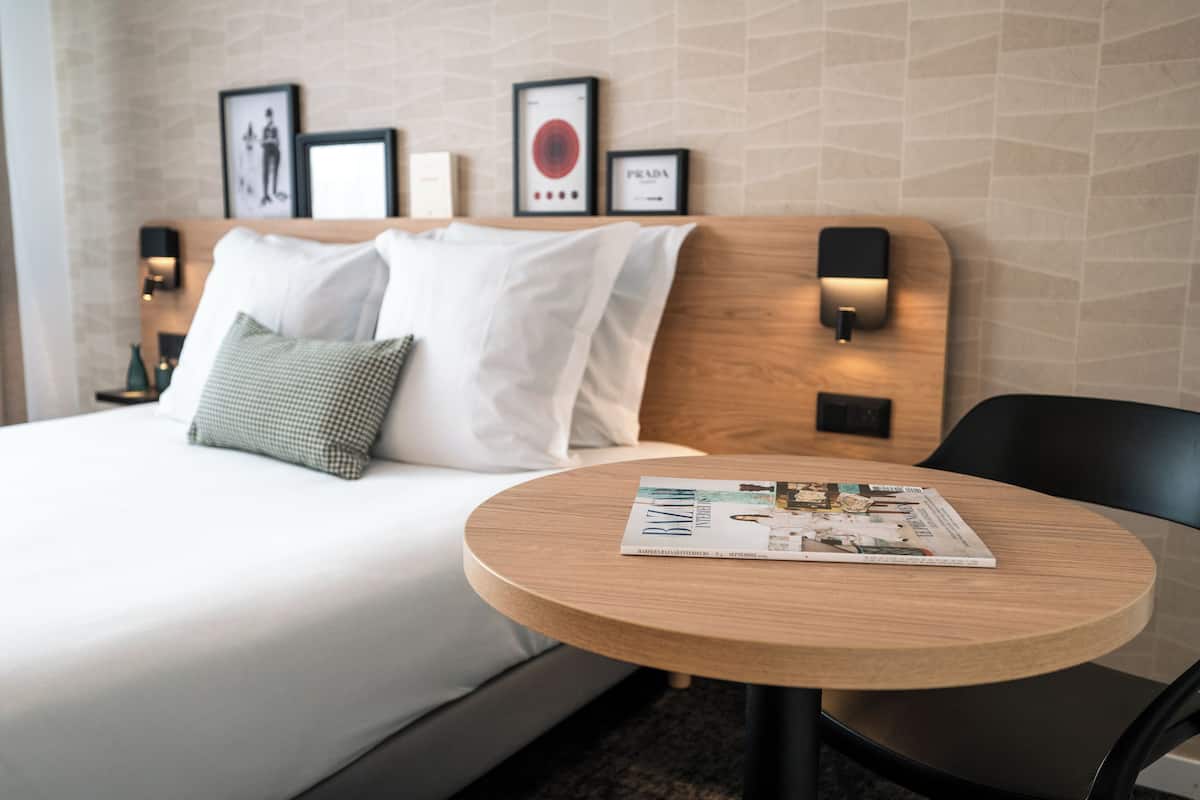 Una habitación de hotel con una cama, una mesa redonda de madera y cuadros en la pared.